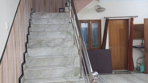 A staircase with marble steps and metal railings, leading to a landing with a wooden door and a window with curtains.