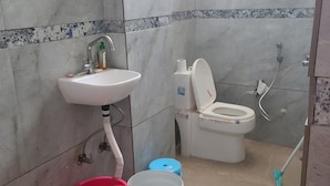 A bathroom with a sink, toilet, and a mop. There are buckets and a container on the floor.