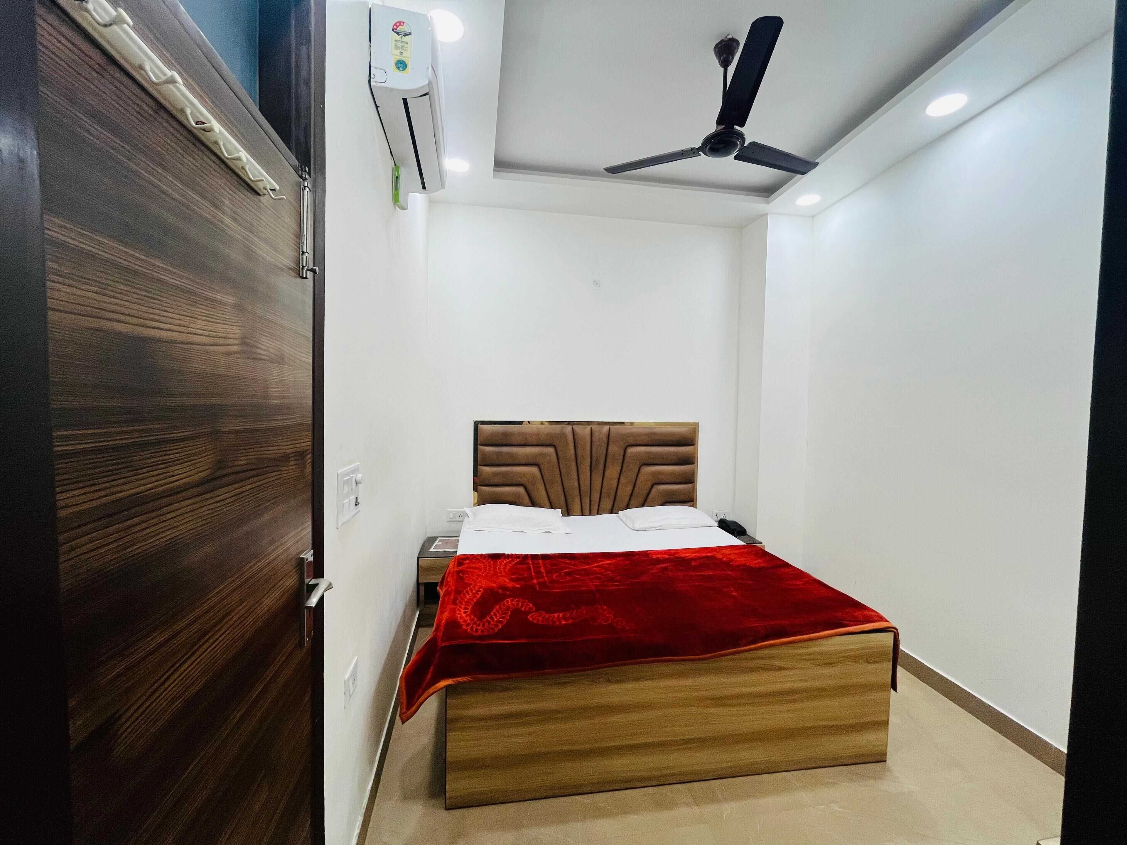 A bedroom with a wooden bed, a red blanket, a ceiling fan, and an air conditioning unit.