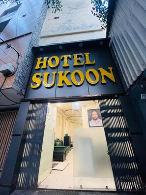 Une enseigne d’hôtel portant le nom « HOTEL SUKOON », et un aperçu de l’intérieur, notamment le comptoir de réception et l’espace salon.