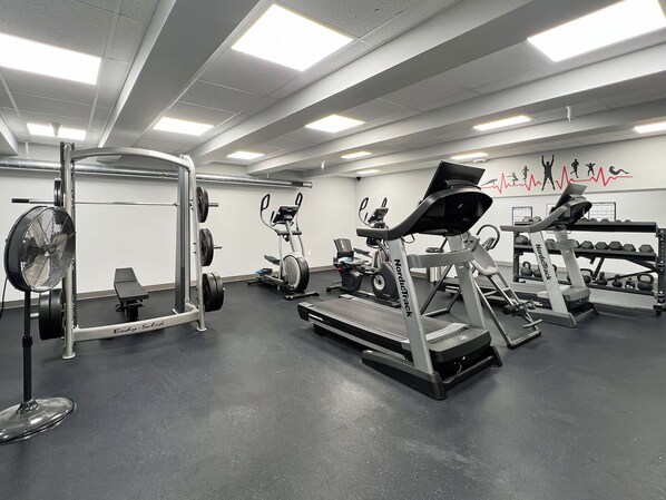Un gimnasio con cintas de correr, máquinas de pesas y un ventilador.