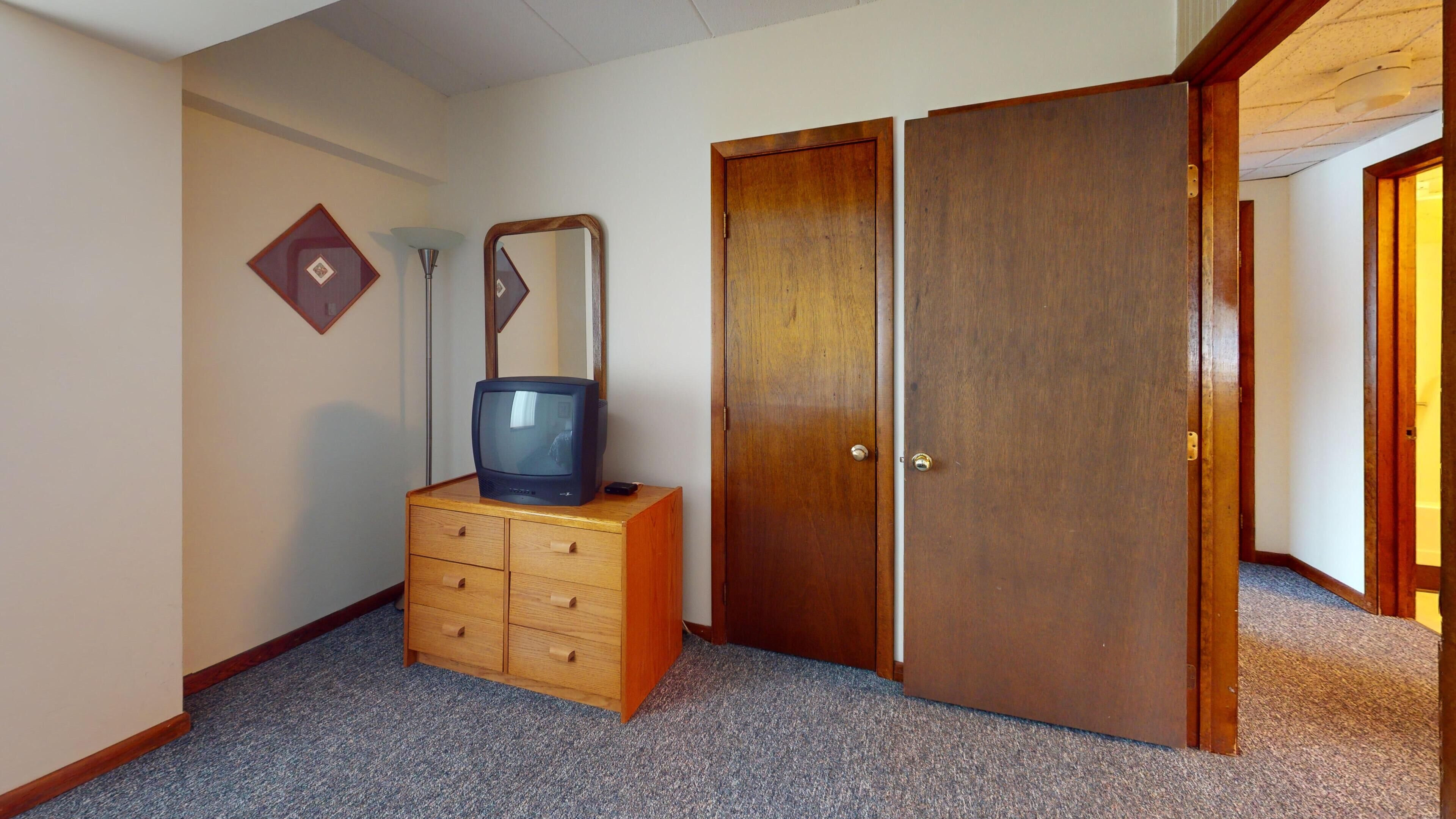 Una habitación con un aparador de madera, televisor, espejo y una puerta.
