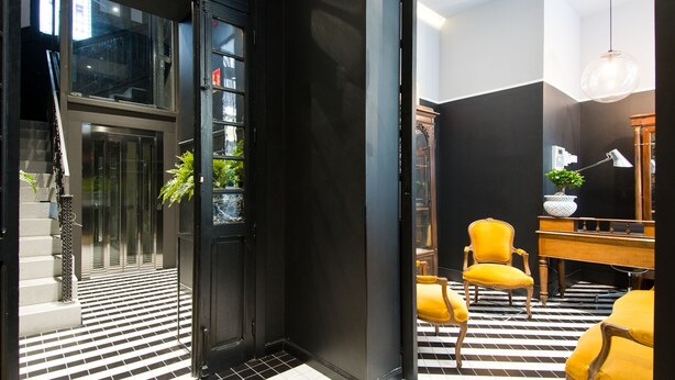 A hotel lobby with a checkered floor, a staircase, a reception desk, and a yellow armchair. - Design Apartment in Barrio de las Letras A1I (Madrid)