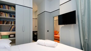 A modern hotel room with a neatly made bed, a television mounted on the wall, and a bookshelf filled with books. - Design Apartment in Barrio Las Letras A02I (Madrid)