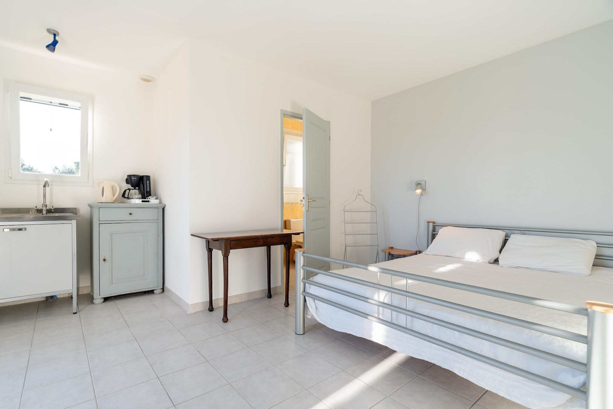 Une chambre à coucher comprenant un lit, un bureau, une chaise, un petit meuble et une fenêtre.