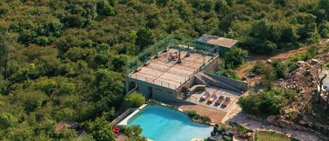 An aerial view of a resort with a swimming pool, lounge chairs, and a small building.