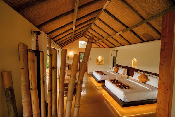 Una habitación con techo alto, columnas de bambú y una cama con cabecera.
