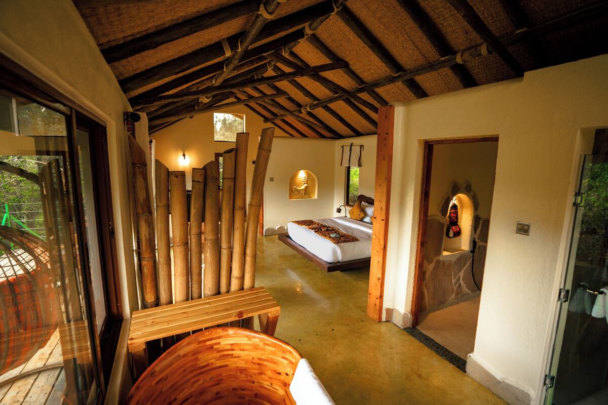 Quarto com cama, mesa de madeira e porta de vidro que dá para o exterior.