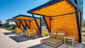 Un área de estar al aire libre con bancos y mesas de madera, bajo una estructura de pérgola de madera.
