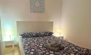 Una cama con una colcha estampada, dos lámparas de noche y un adorno en la pared.
