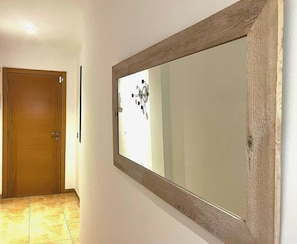 Un pasillo con una puerta de madera, un espejo grande y un accesorio de luz en la pared.
