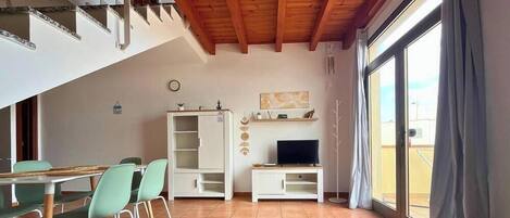 A dining area with a table and chairs, a white cabinet, a television, and a large window with curtains.