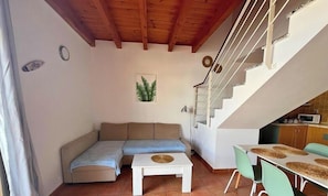 Un espace de vie chaleureux comprenant un canapé, une petite table, un escalier et un coin cuisine.