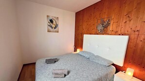 Ett sovrum med en säng, ett sängbord, ett konstverk som hänger på väggen och en väggpanel av trä.