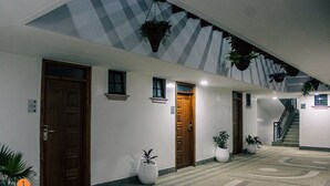 Un hall d’hôtel avec un plafond à carreaux, de nombreuses portes, des plantes en pot et un escalier.