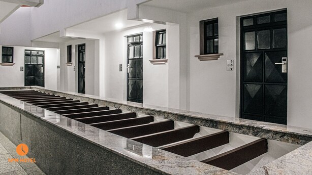 Un couloir d’hôtel moderne, avec un long escalier droit menant à plusieurs portes, chacune surmontée d’une petite fenêtre.