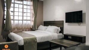 Une chambre d’hôtel avec un lit, une table de chevet, une télévision et des rideaux.
