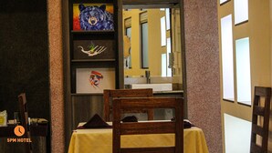 Une chambre d’hôtel avec une chaise en bois, une table recouverte d’une nappe jaune et des œuvres d’art accrochées au mur.