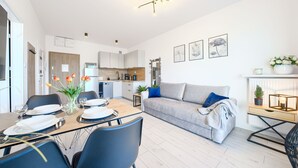 A modern living room with a grey sofa, a dining table set for four, and a kitchen in the background. - Apartamenty Sun & Snow Pelikan (Rewal)