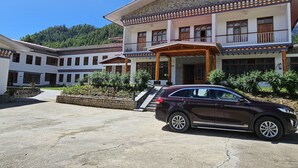 Un immeuble à plusieurs étages, doté d’une façade en pierre, d’une entrée couverte et d’un espace de stationnement où se trouve une voiture.