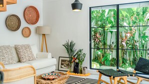 A modern living room with a white sofa, a black and white striped rug, a wooden coffee table, and a black lounge chair. There is a large window with a view of tropical plants. - Mare Villa by Betterplace (Canggu)