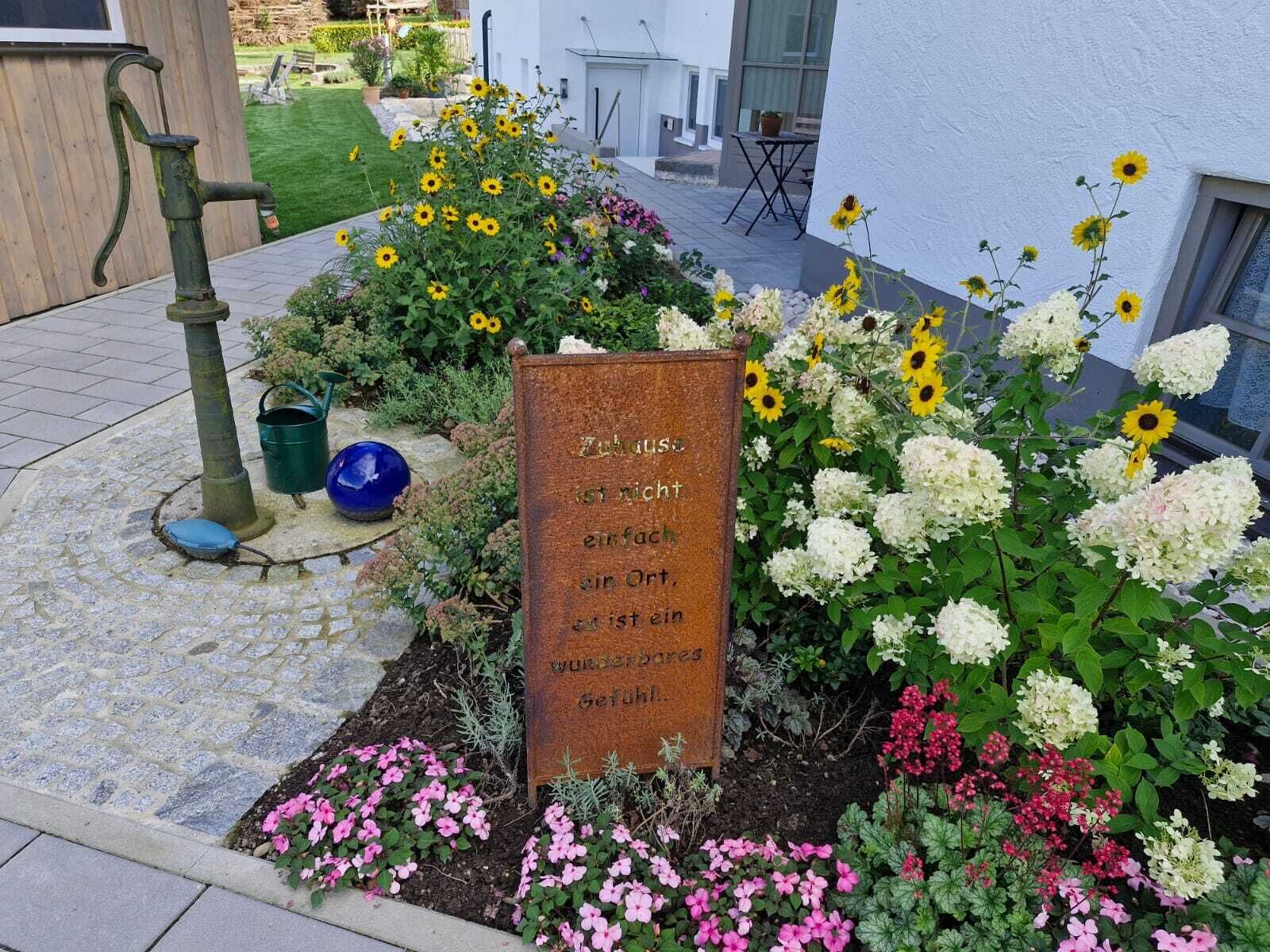 A garden with a sign, flowers, and a water fountain.
