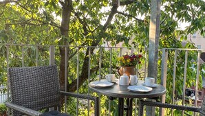 A wooden deck with wicker furniture and a table set for two, surrounded by lush greenery. - Gemütliche Ferienwohnung am Kirschbaum in Malschwitz in der Oberlausitz (Malschwitz)