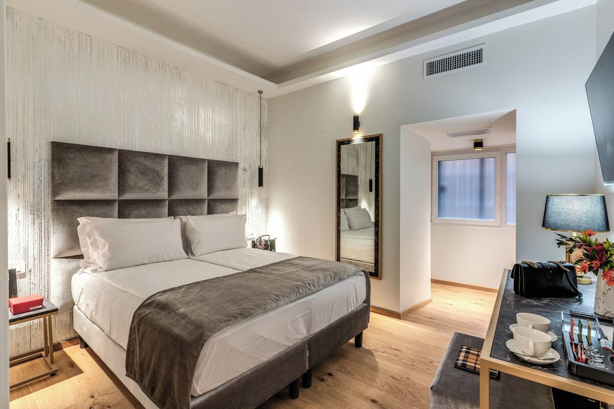 Een moderne slaapkamer met een groot bed, nachtkastjes, een spiegel, een bureau met lamp en een raam.