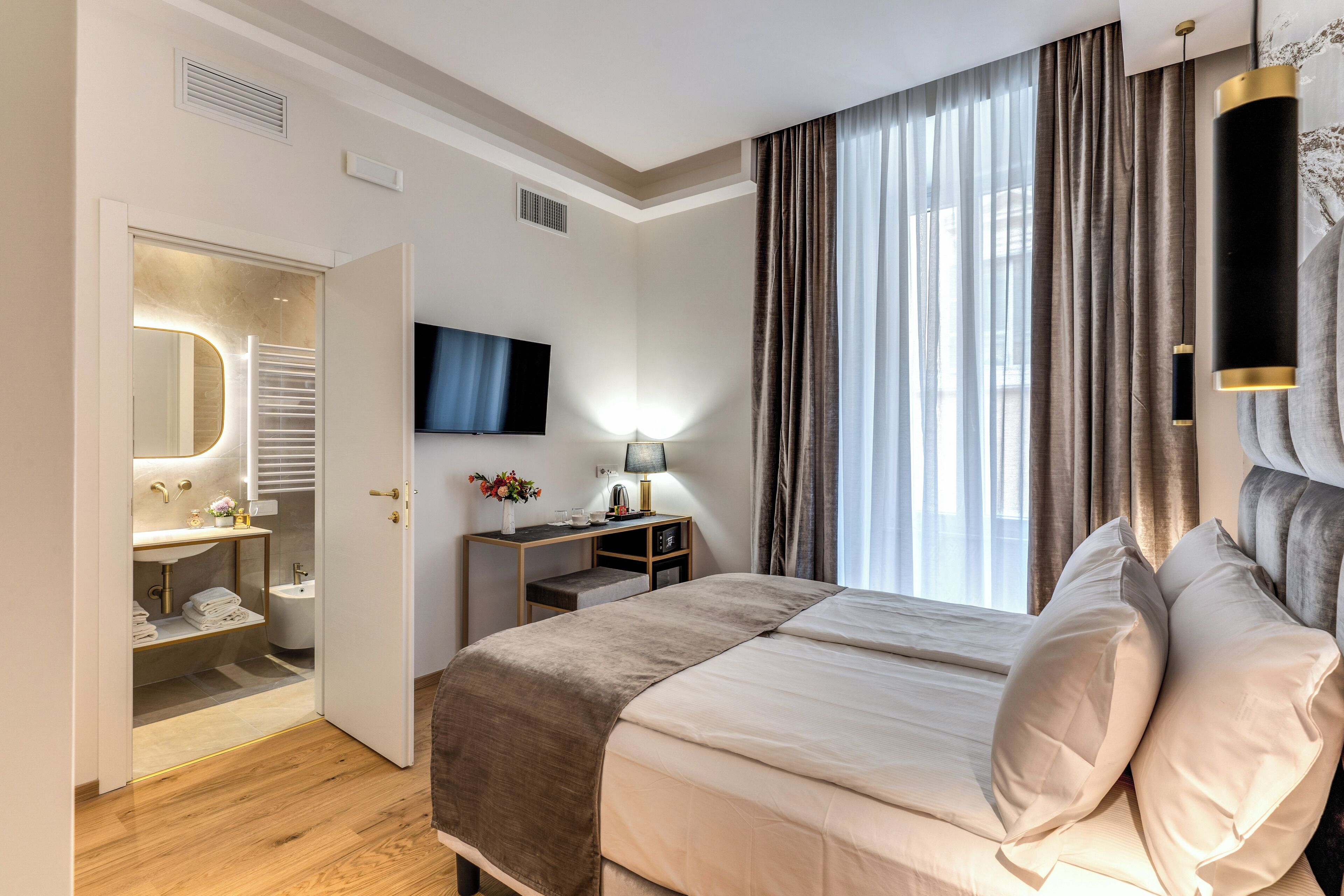 A hotel room with a large bed, a television, a desk with a lamp, and a bathroom with a mirror and sink.