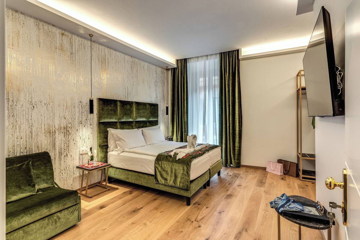 Een hotelkamer met een bed, een groene bank, een kleine tafel en een aan de muur bevestigde televisie.