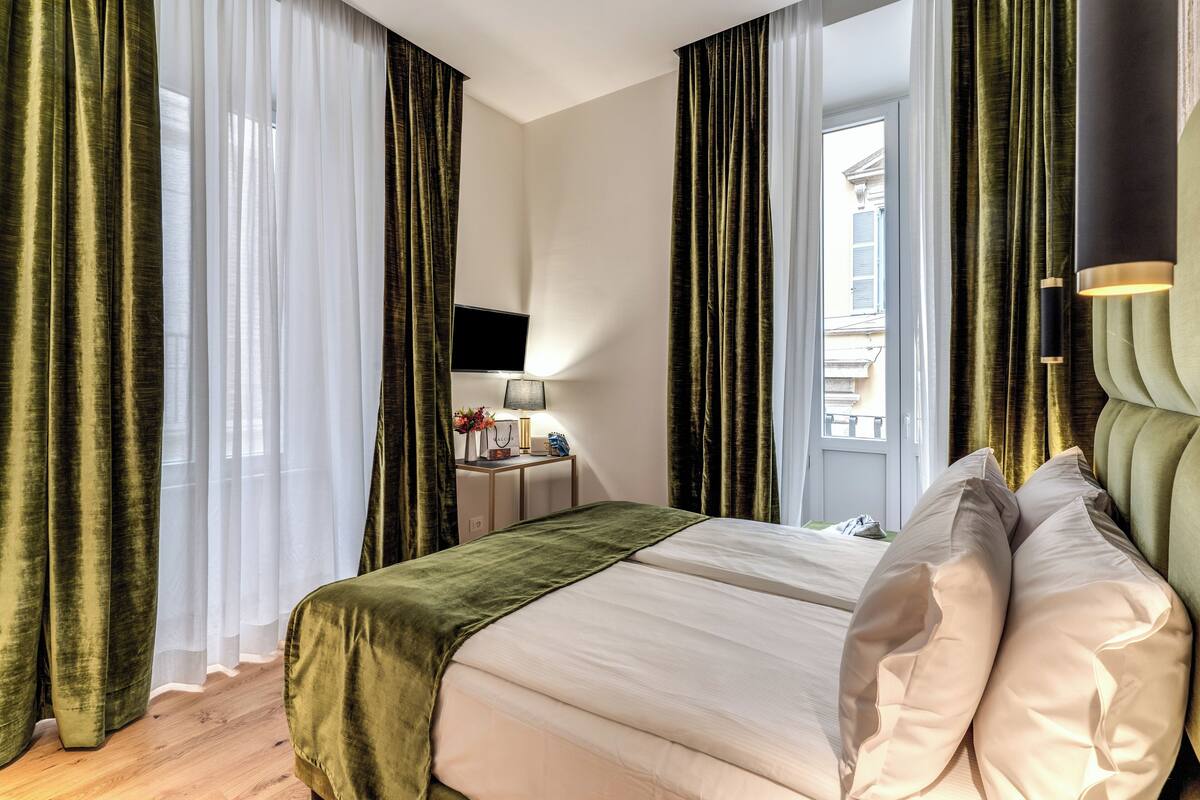 Een hotelkamer met een bed, een televisie, een bureau met lamp en gordijnen.
