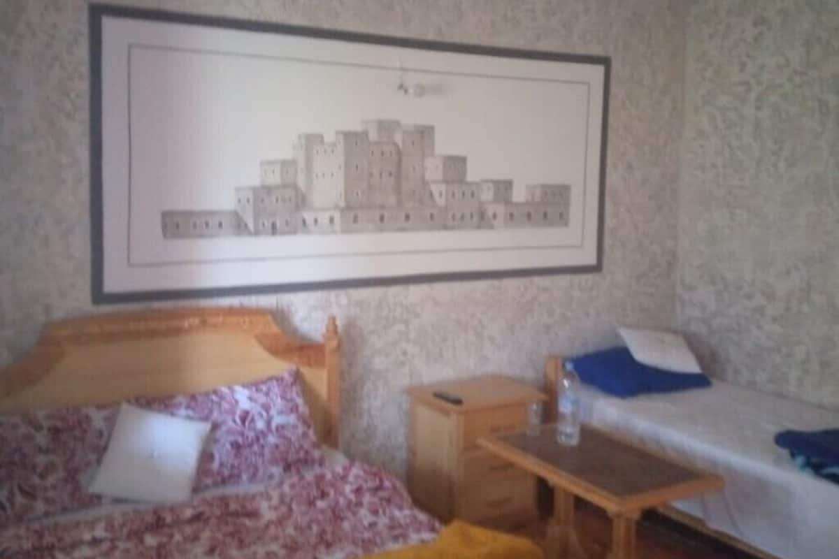 A bedroom with a bed, a bedside table, a small desk, and a framed picture on the wall.