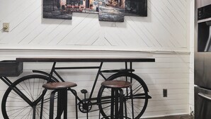 Ett kök med en vit trävägg, en bardisk med cykeltema och barstolar samt ett kylskåp i rostfritt stål.