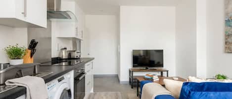 A modern kitchen with a washing machine, a dining area with a blue sofa, and a TV.