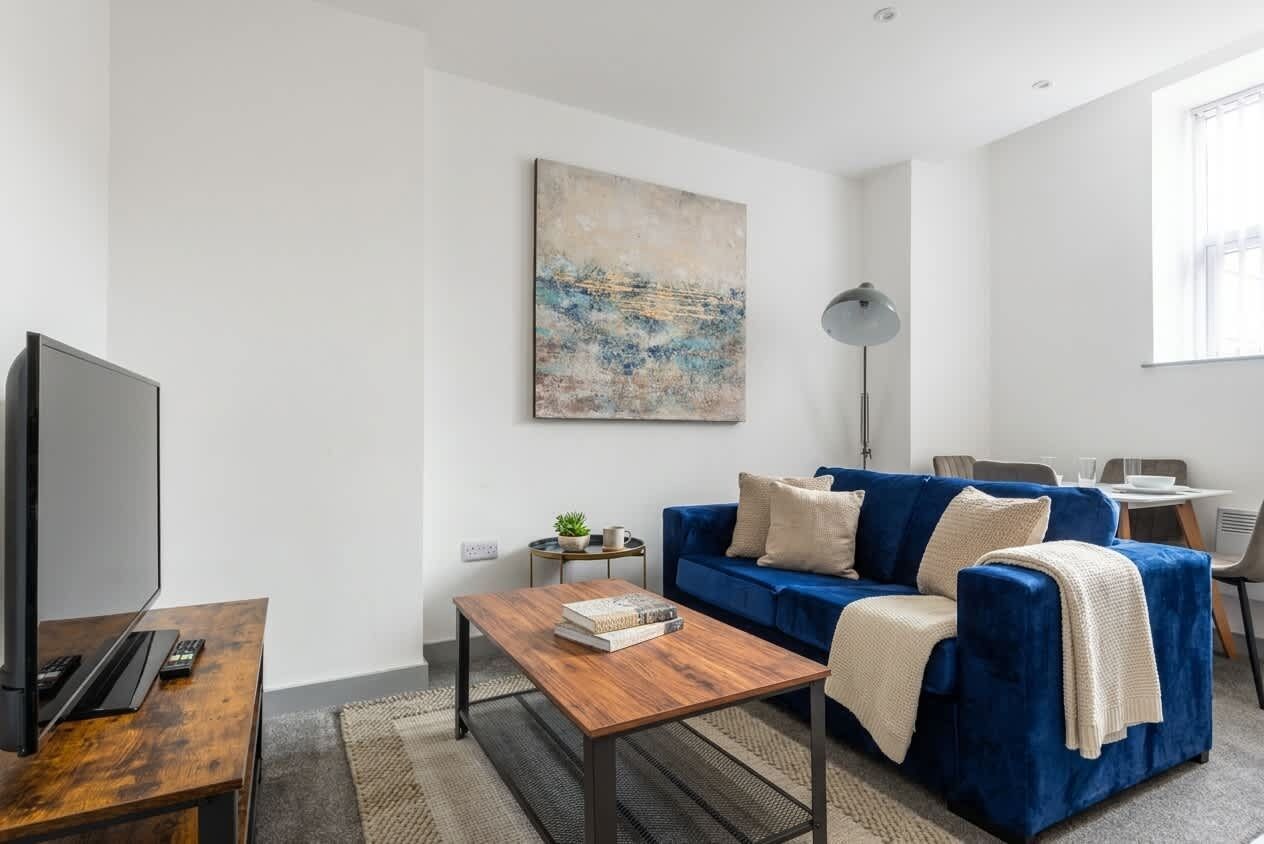 A modern living room with a blue sofa, a coffee table, a flat-screen TV, and a painting on the wall.