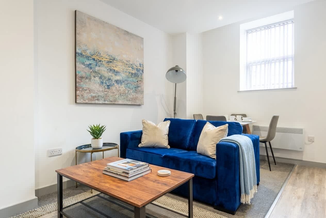 Ein modernes Wohnzimmer mit einem blauen Sofa, einem Couchtisch, einem Gemälde und einem Fenster mit Jalousien.