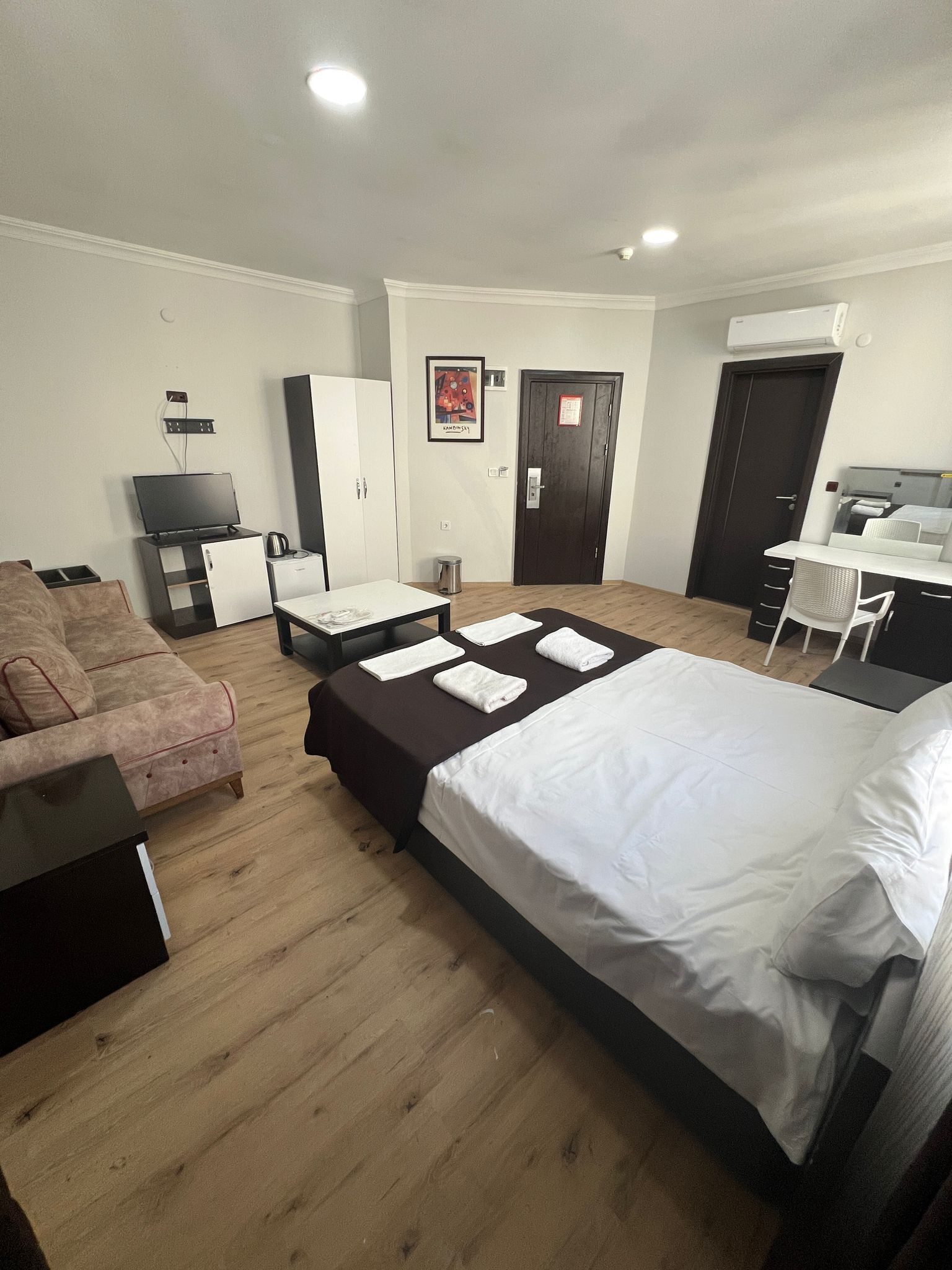 A hotel room with a bed, a sofa, a desk, a chair, a television, and a door.