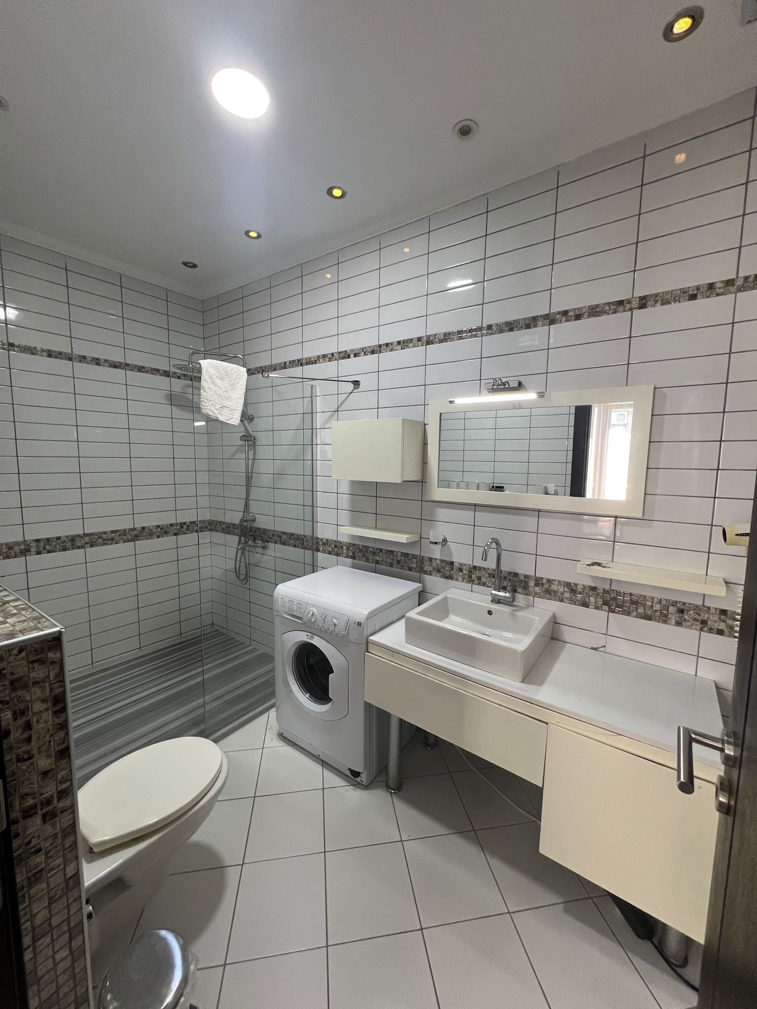Un baño moderno con inodoro, lavadora, lavabo y ducha.
