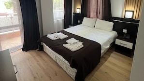 A modern hotel room with a large bed, a bedside table, a desk, and a chair. There is a window with curtains, a ceiling light, and a wall-mounted air conditioner. - KOLİBRY SV HOTEL (Konyaalti)