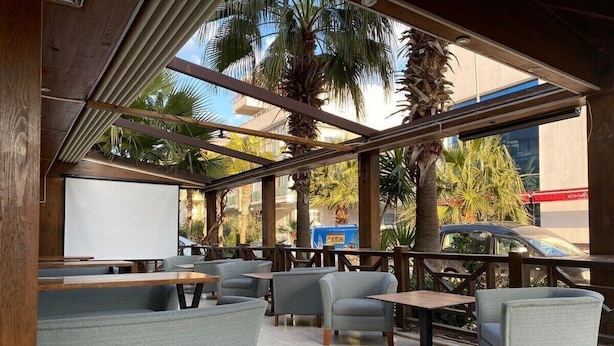An outdoor seating area with cushioned chairs and tables, a whiteboard, and palm trees. - KOLİBRY SV HOTEL (Konyaalti)