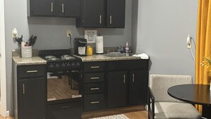 A compact kitchen with dark cabinets, a stove, and a small dining area with a chair and table.