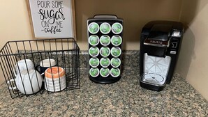 A kitchen counter with a coffee maker, a mug rack, and a sign that reads "pour some sugar on me - coffee".