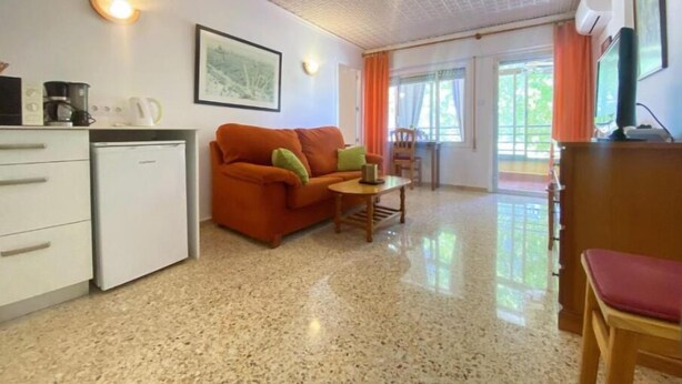 Un espacio habitable compacto con kitchenette, un sofá, una mesa de comedor y una silla.