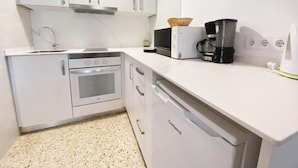 Una cocina con armarios blancos, horno de acero inoxidable, microondas y cafetera.