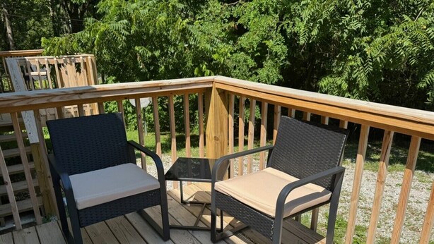 Una terraza de madera con dos sillas de mimbre y una mesa.