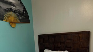 Una cama con colcha estampada con motivos florales, cabecera de madera y un ventilador de pared.