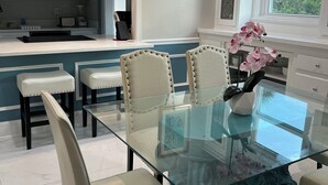 Una cocina moderna con una mesa de comedor de vidrio, sillas blancas y lámparas colgantes.