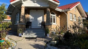 Una casa de dos pisos con fachada de piedra, techo de tejas rojas y un porche con escalones que llevan a una puerta blanca.