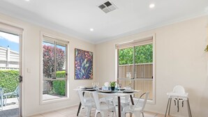 A dining area with a table set for four, white chairs, and a high chair. - Your family & staff will love it here! Bed & bath linen hire included. Unlimited WIFI. Free, easy parking. Free child friendly amenities. Keyless access. Easy self check in. No stairs! (Richmond)