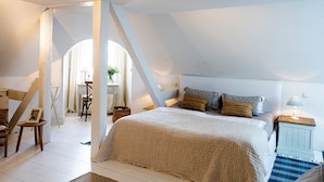 A bedroom with a sloped ceiling, a large bed with multiple pillows, a nightstand with a lamp, and a chair.